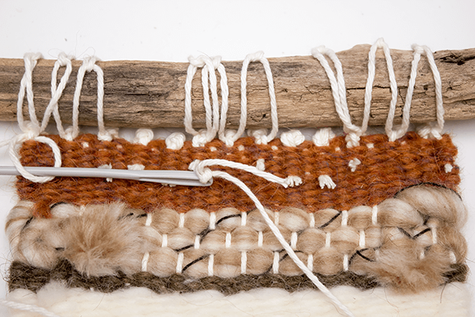 Attaching driftwood to a woven wall hanging.